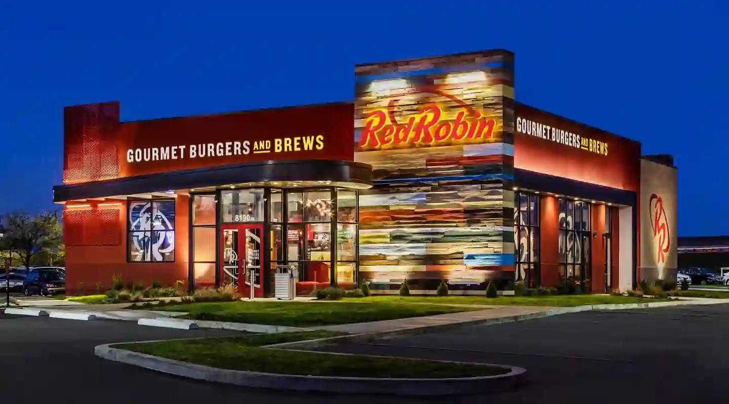 Exterior of Red Robin restaurant with red and wood-toned facade, bold signage reading “Red Robin Gourmet Burgers and Brews,” glass entryway beneath the address 8190, and surrounding landscaping.