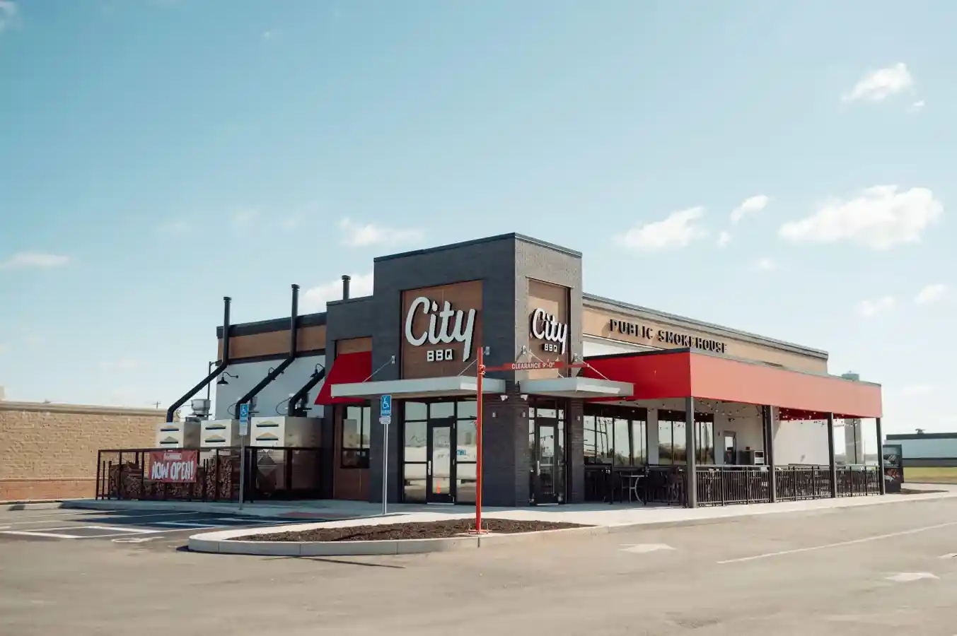 City BBQ restaurant exterior with brick and wood siding, red awning, large signage reading “City BBQ” and “PUBLIC SMOKEHOUSE,” and a “NOW OPEN” banner above the entrance, set against a sunny sky.