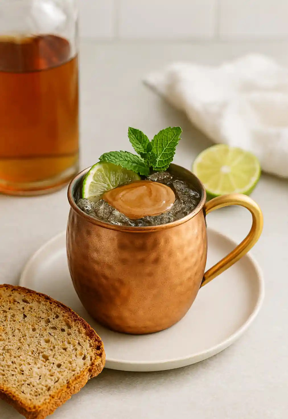 Kentucky Mule recipe cocktail served in a copper mug with ice, lime wedge, and mint sprig on a marble countertop.